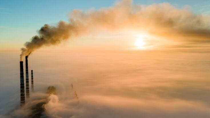 Aerial view of coal power plant high pipes with black smoke moving up polluting atmosphere at sunset.