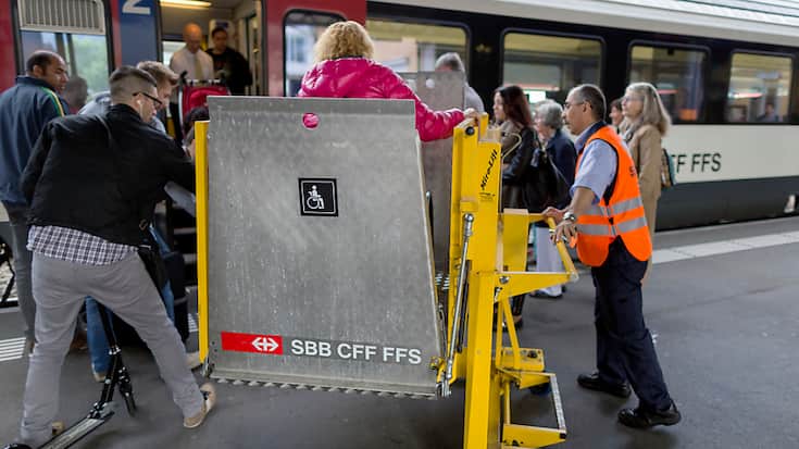 Un employé des CFF,  à l'aide d'un élévateur, permet à une femme en chaise roulante d'accéder à un train.