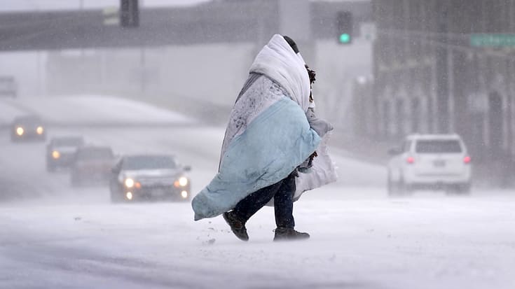 Une personne enveloppée dans une couverture traverse une rue couverte de neige à St. Louis, dans le MIssouri.