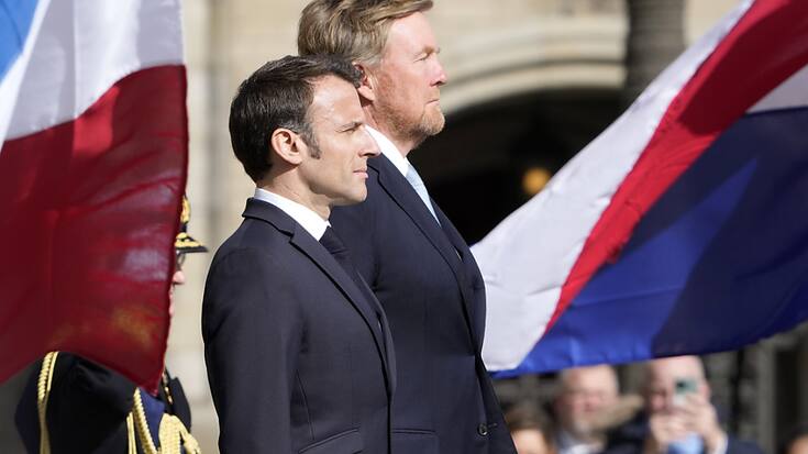 Emmanuel Macron et le roi Willem-Alexander devant les drapeaux de leurs pays qui partagent les mêmes couleurs dans un sens différent.