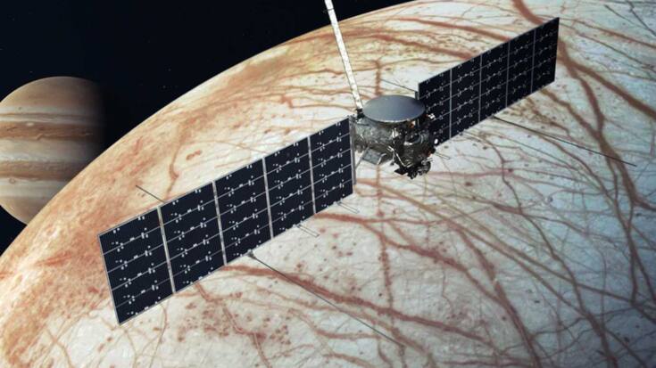 Une image de la NASA avec le vaisseau spatial Europa Clipper au-dessus de la lune, Europa, avec Jupiter à l'arrière-plan à gauche.