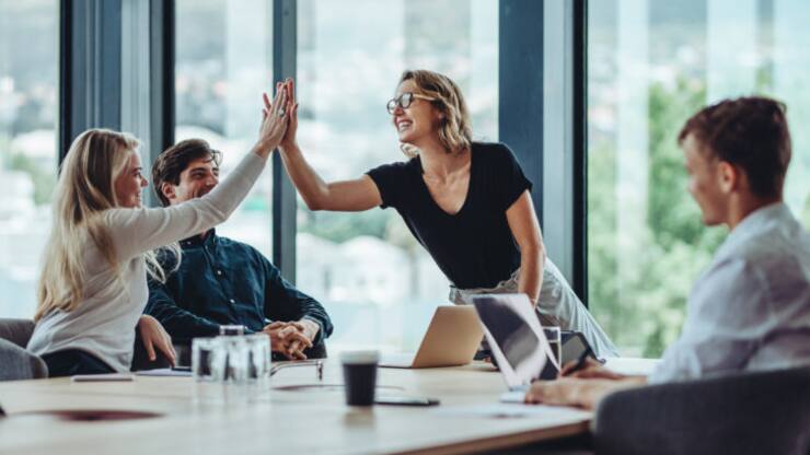 Female professional giving a high five to her colleague in conference room. Group of colleagues celebrating success in a meeting.