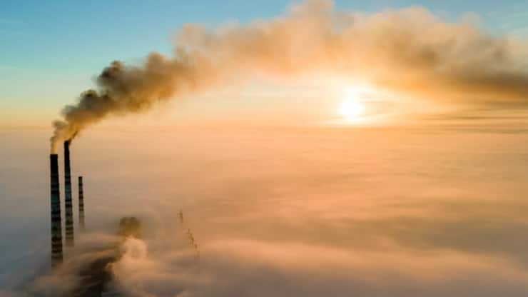 Aerial view of coal power plant high pipes with black smoke moving up polluting atmosphere at sunset.
