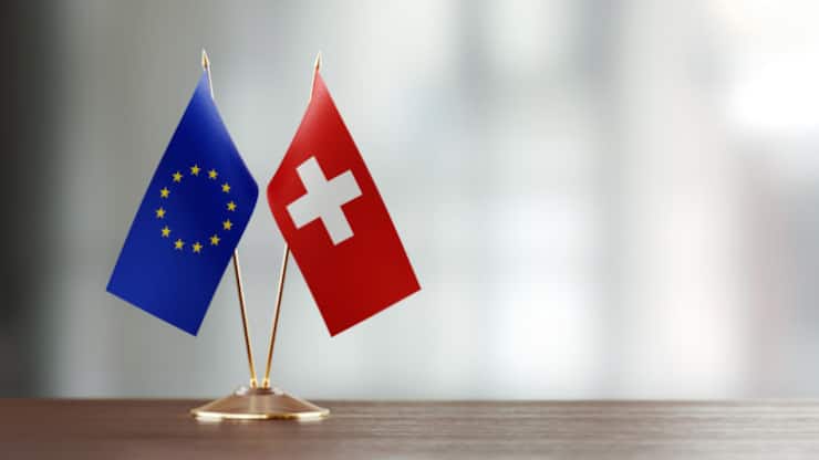 European Union and Swiss flag pair on desk over defocused background. Horizontal composition with copy space and selective focus.