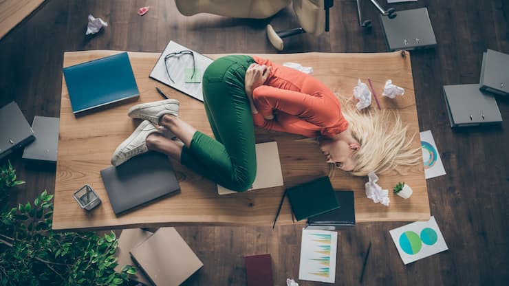 High angle above view photo of corporate messy atmosphere unorganized, blond business lady lying table suffering period pms holding hurt belly wear casual outfit indoors