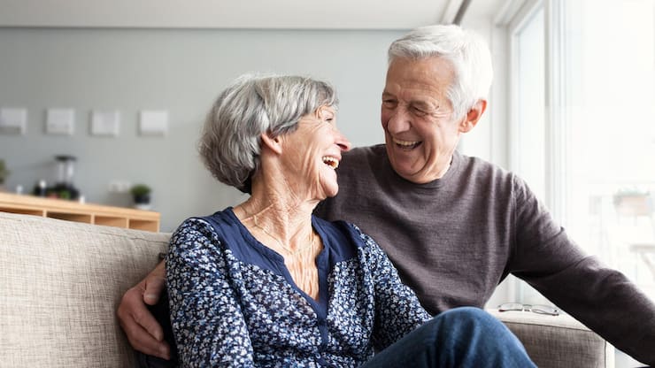 Couple senior heureux assis sur canapé dans salon lumineux - prévoyance retraite