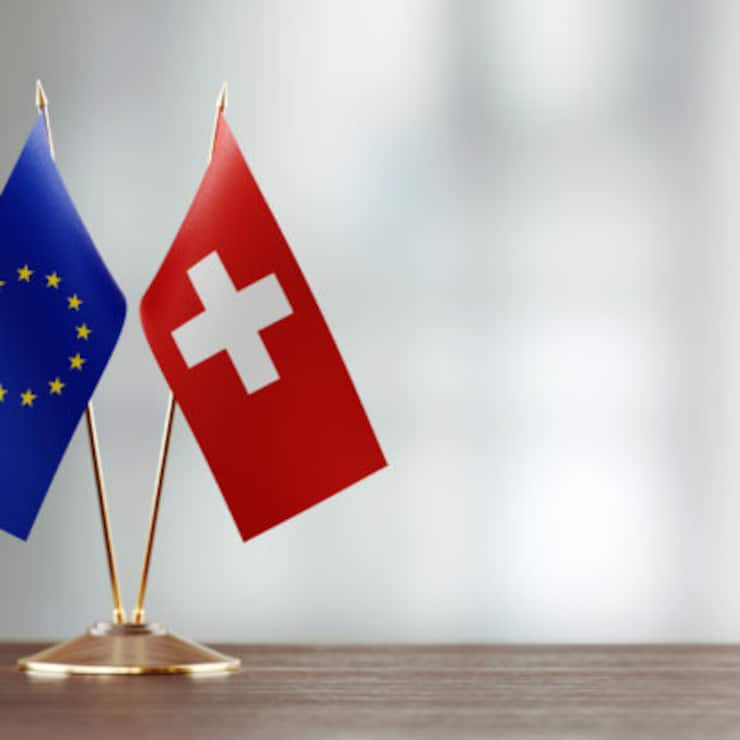 European Union and Swiss flag pair on desk over defocused background. Horizontal composition with copy space and selective focus.