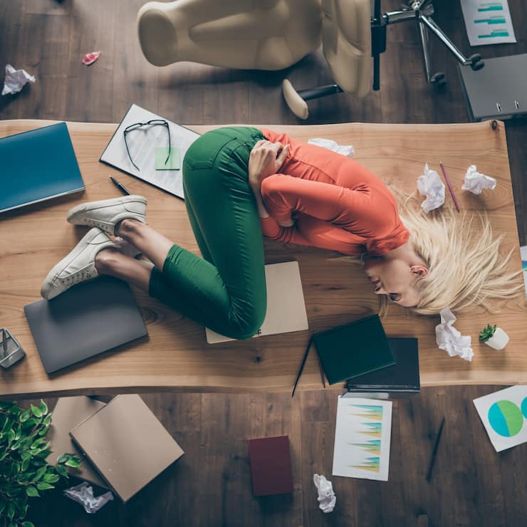 High angle above view photo of corporate messy atmosphere unorganized, blond business lady lying table suffering period pms holding hurt belly wear casual outfit indoors