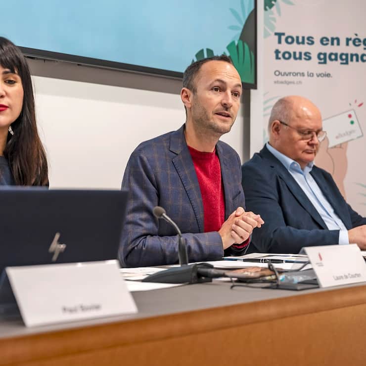Laure de Courten, Cheffe de l'inspection cantonale de l'emploi et de l'aide sociale, Mathias Reynard, Conseiller d'Etat valaisan, Niklaus Furger, representant des Communes, de gauche a droite, parlent lors d'une conference de presse sur le dispositif eBadges, un nouveau systeme de contrele individuel des travailleurs sur les chantiers le vendredi 6 decembre 2024 a Sion. (KEYSTONE/Jean-Christophe Bott)