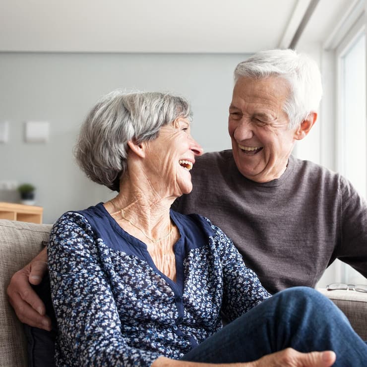 Couple senior heureux assis sur canapé dans salon lumineux - prévoyance retraite