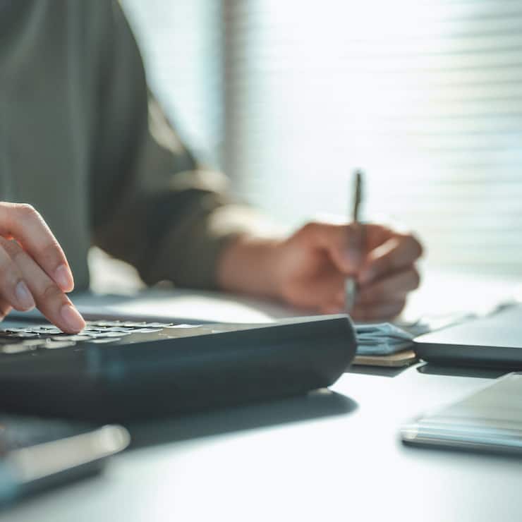Close-up of hands using a calculator and writing on financial documents, representing budgeting, tax management, cost analysis, and professional accounting processes.